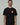 Black Red Shield Elite Mens Tee shown on a male model standing front-facing, featuring the red Gracie Barra Red Shield emblem on the left chest and red sleeve tag against a light gray background.