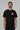 Black Red Shield Elite Mens Tee shown on a male model standing front-facing, featuring the red Gracie Barra Red Shield emblem on the left chest and red sleeve tag against a light gray background.