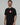 Black Red Shield Elite Mens Tee shown on a male model in a left-facing pose, featuring the red Gracie Barra Red Shield emblem and red sleeve tag against a light gray background.