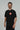 Black Red Shield Elite Mens Tee shown on a male model in a left-facing pose, featuring the red Gracie Barra Red Shield emblem and red sleeve tag against a light gray background.