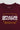 Close-up of puff print "Gracie Barra" logo in white with yellow "Brazilian Jiu-Jitsu" text on maroon fabric.